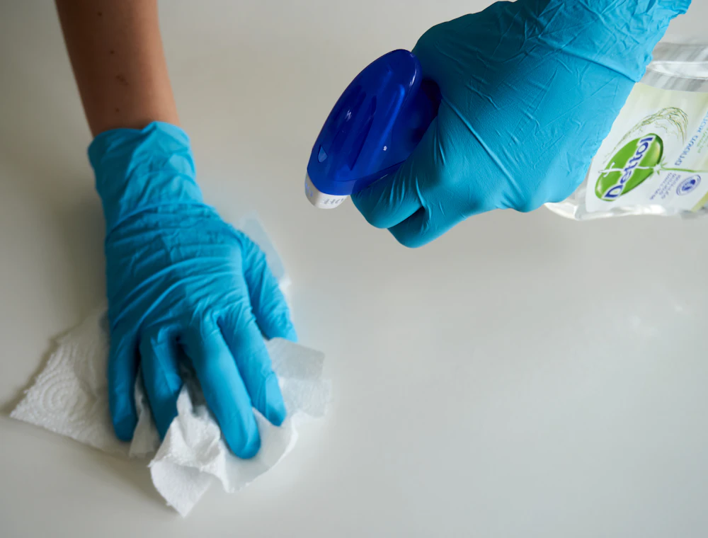 Gloved hands wiping a surface with cleaning spray